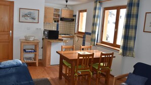 Eine kompakte Küche mit Holzschränken, einem Esstisch mit Stühlen, einem kleinen Kühlschrank und einer Mikrowelle.