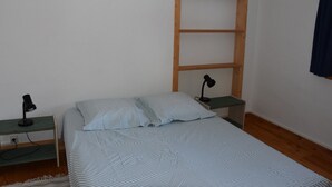 Ein kleiner, schlichter Raum mit einem Bett, zwei Nachttischen und einer Holzleiter an der Wand.