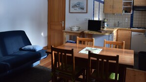 Ein kompakter Wohnbereich mit Essplatz, einer Couch, einem Fernseher und einer Küchenzeile mit Holzschränken und einer gefliesten Spritzschutzwand.