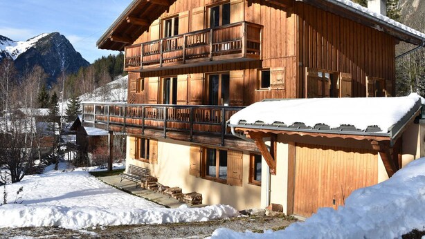 Eine Holzhütte mit Balkon, vor einer Berglandschaft gelegen.