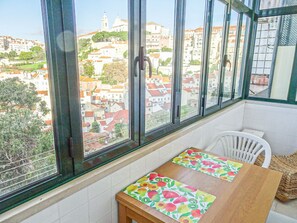 Una habitación con un ventanal que ofrece vistas a un paisaje urbano, una mesa de madera con un mantel individual y una silla blanca.