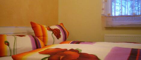 Una cama con ropa de cama y almohadas estampadas con motivos florales, una ventana con vistas a árboles y un radiador.