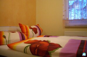 Una cama con ropa de cama y almohadas estampadas con motivos florales, una ventana con vistas a árboles y un radiador.