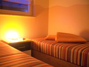 Habitación de hotel con dos camas, una mesita de noche con lámpara y ventana con vistas.