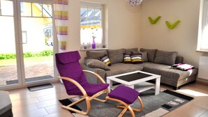 A living room with a sofa, a rocking chair, a coffee table, and a window with curtains. - 3 room first floor - Apartment Ferienhaus Müritzwelle - Ferienwohnungen / (Röbel/Müritz)
