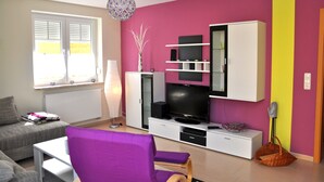 A living room with a sofa, a purple chair, a TV, and a cabinet. - 3 room first floor - Apartment Ferienhaus Müritzwelle - Ferienwohnungen / (Röbel/Müritz)