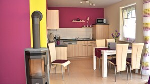 A compact kitchen with a wood-burning stove, a microwave, and a dining area with chairs and a table. - 3 room first floor - Apartment Ferienhaus Müritzwelle - Ferienwohnungen / (Röbel/Müritz)