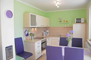 Eine kompakte Küche mit Mikrowelle, Kaffeemaschine und Spüle. Es gibt Stühle und einen Esstisch mit einem Blumenstrauß.