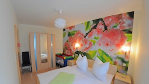 Et hotelværelse med en seng, et natbord, en stol, et klædeskab og en væg med et blomstermaleri.