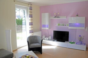 Ein Wohnzimmer mit Fernseher, Sessel und Sofa.