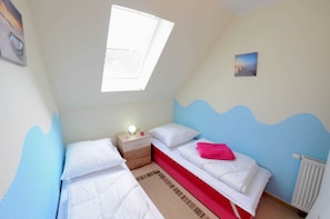 A bedroom with two beds, a nightstand, a window, and a radiator.