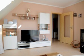 Un salon doté d’un téléviseur à écran plat, d’un meuble de rangement blanc, d’étagères en bois et d’une porte donnant sur une autre pièce.