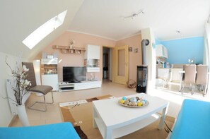 Un salon moderne doté d’un téléviseur à écran plat, d’un coin repas avec une table et des chaises, et d’une cuisine en arrière-plan.