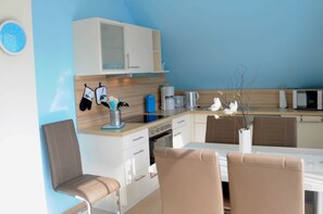 Une cuisine moderne avec des meubles blancs, un four à micro-ondes et une machine à café. On y trouve deux chaises et une table à manger.