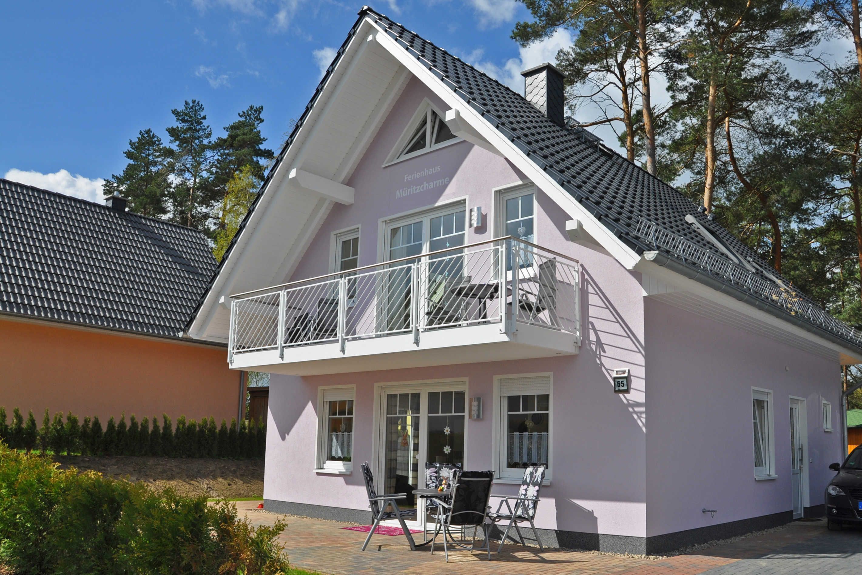 A two-story building with a balcony, a visible entrance, and a paved outdoor area with chairs and a table.