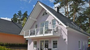 Un bâtiment à deux étages doté d’un balcon, d’une entrée bien visible et d’un espace extérieur aménagé avec des chaises et une table.