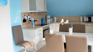 A modern kitchen with white cabinets, a microwave, and a coffee maker. There are two chairs and a dining table. - 3 room upper floor - Apartment Ferienhaus Müritzcharme - Ferienwohnungen / (Röbel/Müritz)