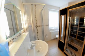 Une salle de bain moderne avec un grand miroir, un lavabo, un espace douche et une porte de douche en verre.