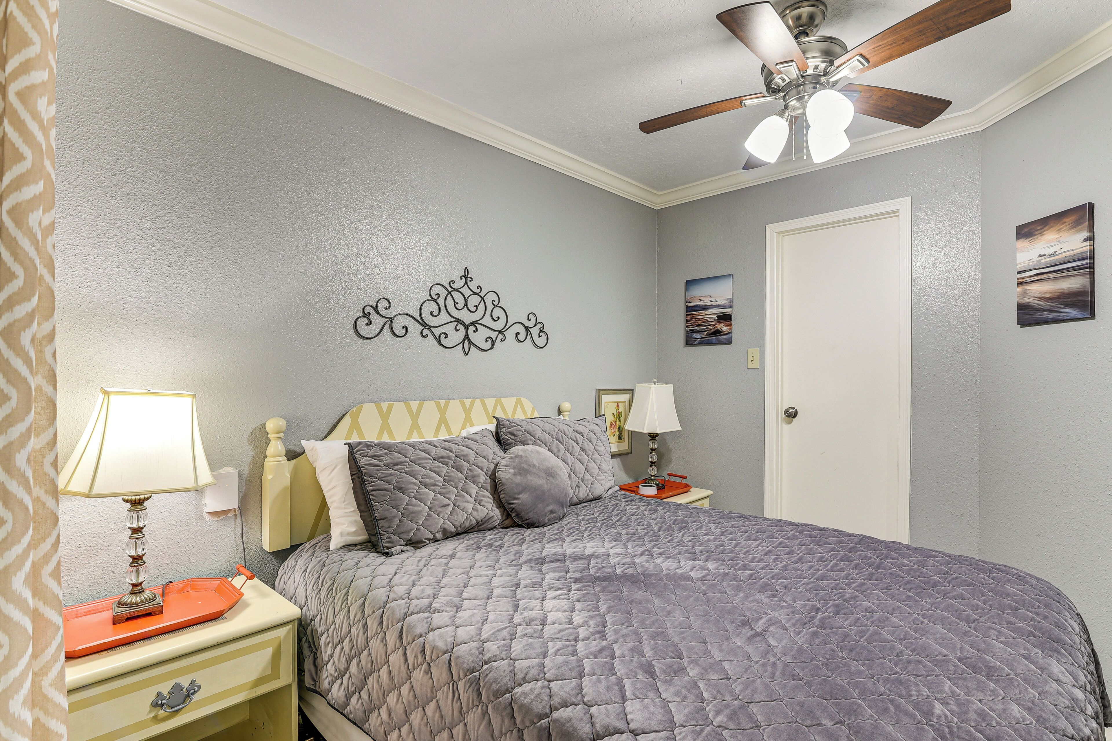Une chambre à coucher comprenant un lit, des tables de chevet, des lampes, un ventilateur de plafond, un élément décoratif mural et une porte.