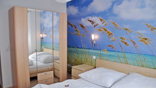 A bedroom with a bed, a nightstand, a dresser, and a mirror. - 3 room first floor - Apartment Ferienhaus Müritzbrise - Ferienwohnungen / (Röbel/Müritz)