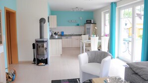 A modern living room with a fireplace, a dining area, and a kitchen with a blue accent wall. - 3 room first floor - Apartment Ferienhaus Müritzbrise - Ferienwohnungen / (Röbel/Müritz)
