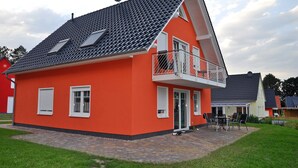A red house with a sloped roof, a balcony, and a paved patio area. - 3 room first floor - Apartment Ferienhaus Müritzbrise - Ferienwohnungen / (Röbel/Müritz)