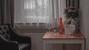 A room with a black leather chair, a wooden table with a bottle of champagne, two wine glasses, and a bouquet of flowers. - City Apartments in Köln am Rheingarten (Cologne)