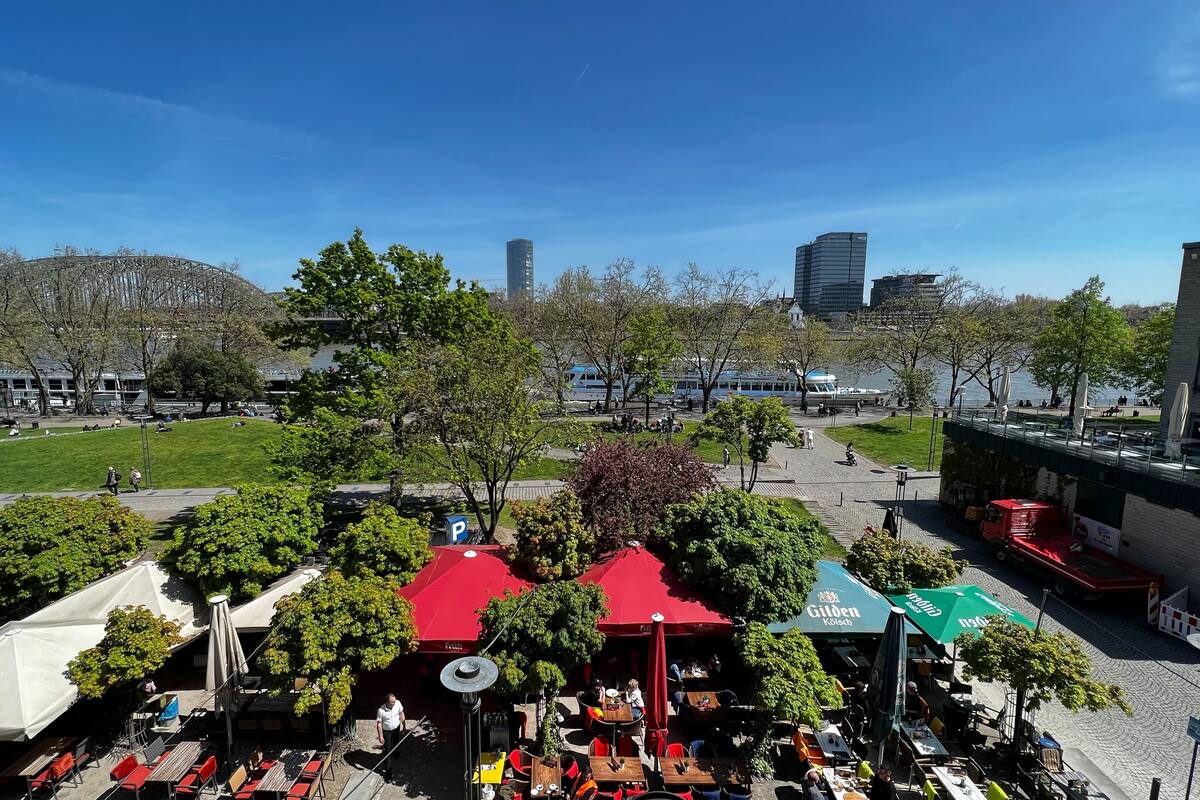 Un espace de café en plein air, avec des tables et des chaises, entouré d’arbres et de bâtiments.