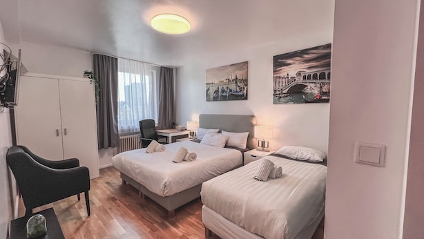 A hotel room with two beds, a desk, a chair, and a radiator. - City Apartments in Köln am Rheingarten (Cologne)