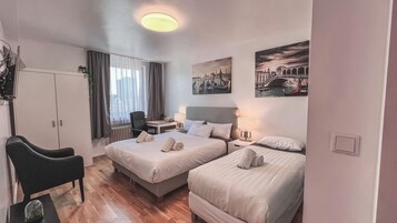 Habitación de hotel con dos camas, un escritorio, una silla y un radiador.