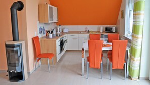 A compact kitchen with a stove, microwave, and sink. There are orange chairs around a small dining table. - 3 room upper floor - Apartment Ferienhaus Müritzbrise - Ferienwohnungen / (Röbel/Müritz)