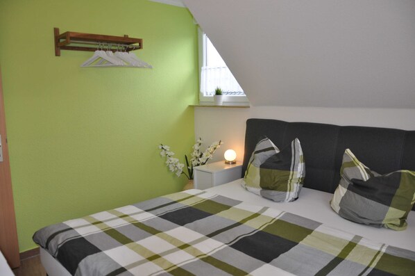 Ein Schlafzimmer mit Bett, Nachttisch, Fenster, Pflanze und einer Kleiderstange.