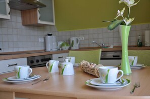En morgenmadsopsætning med hvide og grønne kopper, underkopper og en grøn vase med blomster på et træbord.