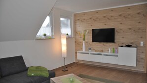 Un soggiorno moderno con un divano grigio, una parete d'accento in legno, una TV a schermo piatto e un mobile console bianco.