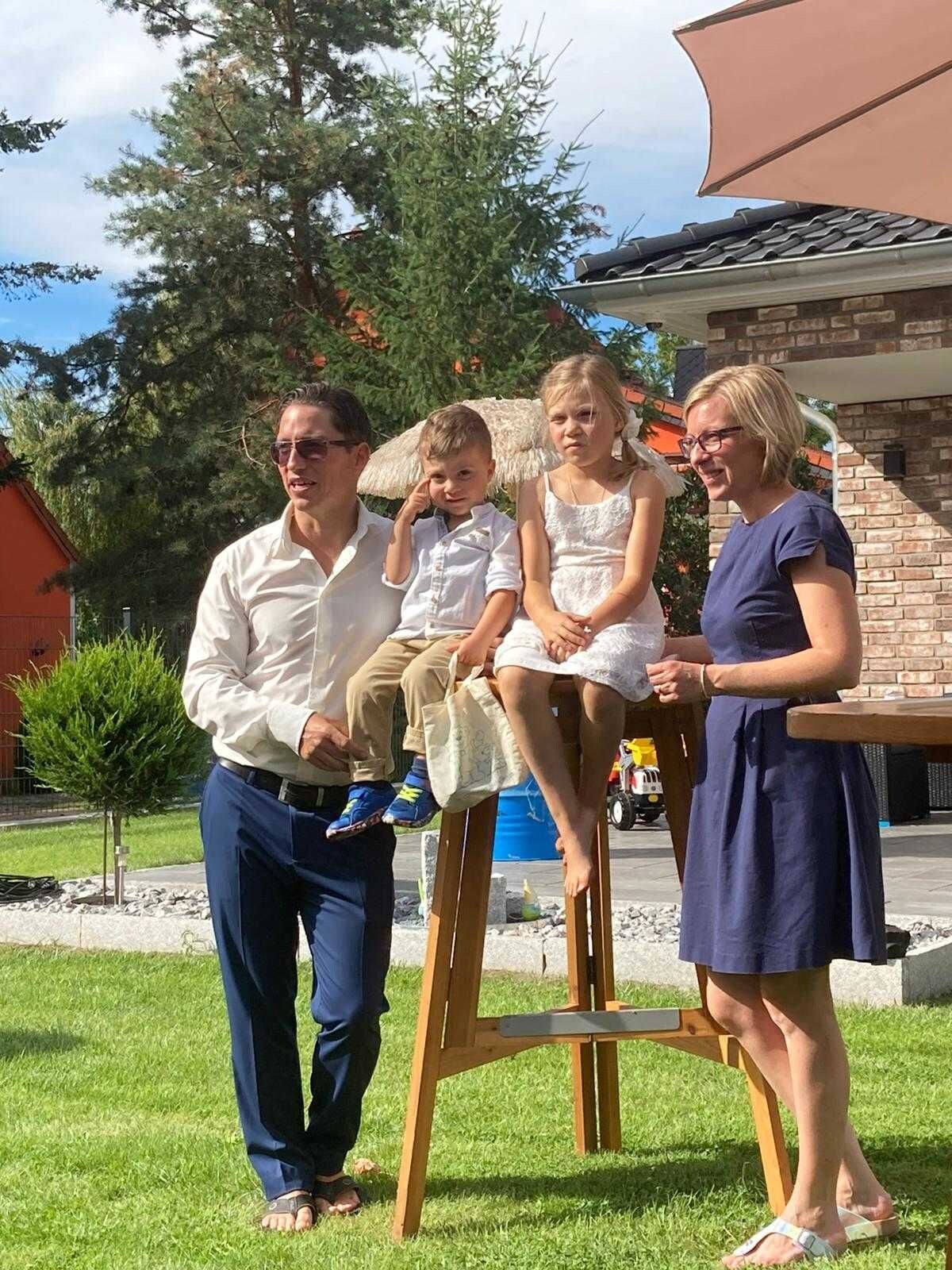 Une famille de quatre personnes, en plein air, avec une maison en arrière-plan.