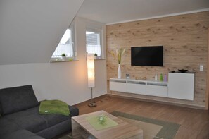 A modern living room with a grey sofa, a wooden accent wall, a flat-screen TV, and a white console unit.