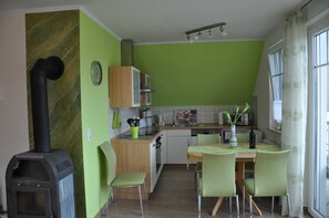 Eine Küche mit Kachelofen, grünen Wänden, einem Esstisch mit Stühlen und einem Fenster mit Vorhängen.
