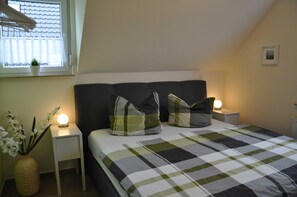 Et soveværelse med en seng, to sengeborde, et natbord med lampe, et vindue med persienner og et billede hængt på væggen.