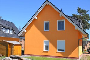Ein zweistöckiges Haus mit einem Satteldach, weißen Fensterrahmen und einer roten Fußleiste.