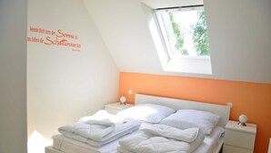 A neatly made bed with white linens, a small bedside table with a lamp, and a window with a view of trees. - 3 room upper floor - Apartment Ferienhaus Müritzsonne - Ferienwohnungen / (Röbel/Müritz)