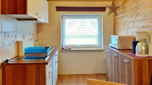 A compact kitchen with wooden cabinets, a window with blinds, a microwave, a coffee maker, and a blue sink.