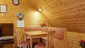 A wooden interior with a wooden table, four chairs, a bench, a clock, and a calendar.