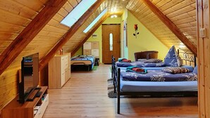 A loft bedroom with a sloped ceiling, wooden beams, a bed, a desk, and a wardrobe.