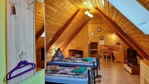 A cozy attic bedroom with two beds, wooden beams, a clock, and a television.