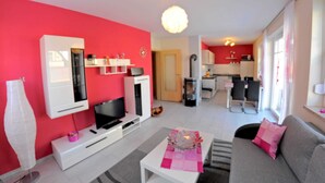 Un salon moderne avec un mur d’accent rouge, un téléviseur à écran plat, un meuble de rangement blanc et un canapé gris.