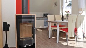 A modern kitchen with a wood-burning stove, white cabinets, and a dining area with a table and chairs. - 3 room upper floor - Apartment Ferienhaus Müritzlust - Ferienwohnungen / (Röbel/Müritz)