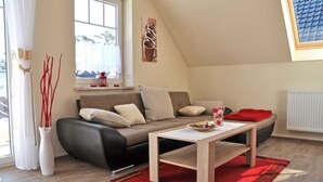 A modern living room with a sofa, a coffee table, and a window with curtains. - 3 room upper floor - Apartment Ferienhaus Müritzlust - Ferienwohnungen / (Röbel/Müritz)