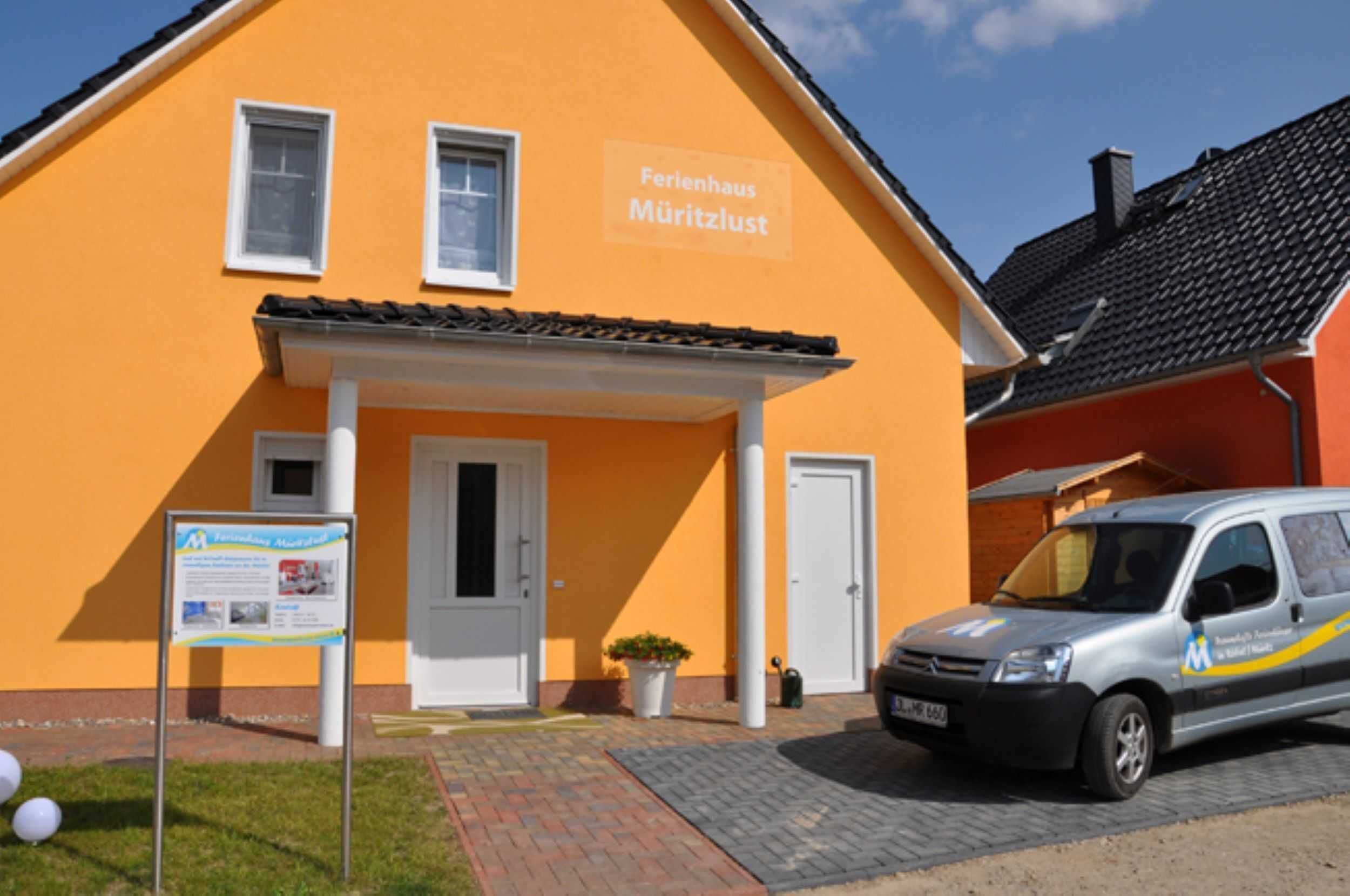 Un edificio con un cartello che riporta "Ferienhaus Müritzlust" e un furgone parcheggiato con un logo.
