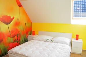 Quarto com cama, mesas de cabeceira brancas e um mural vibrante na parede.