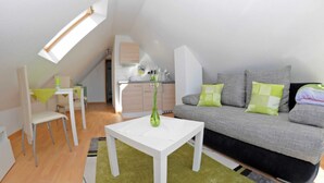 Een moderne, compacte leefruimte met een eethoek, kitchenette en een gezellige zithoek met een bank en kussens.